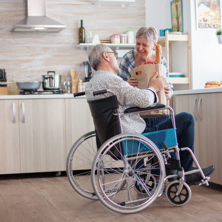 senior-woman-taking-grocery-paper-bag-from-handicapped-husband-wheelchair-mature-people-with-fresh-vegetables-from-market-living-with-disabled-person-with-walking-disabilities